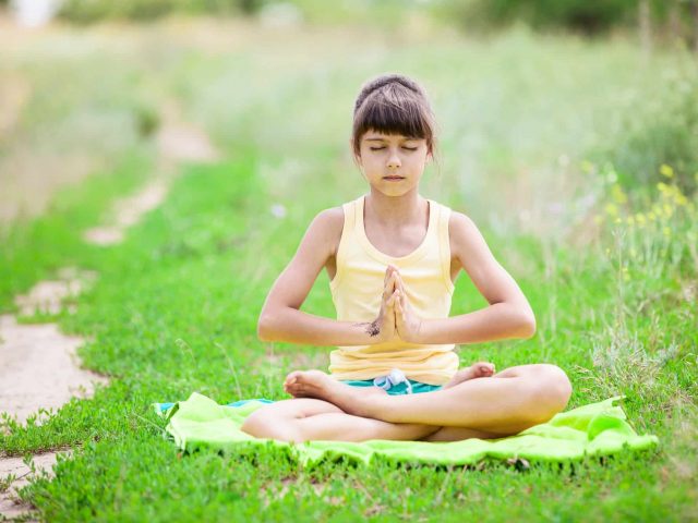 Little girl meditating while sitting in lotus position on grass.